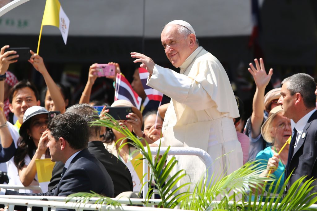 Pope Francis waving to the crowd while on the pope mobile with some Thai flags in the background during his Apostolic Visit to Thailand in 2019