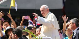Pope Francis waving to the crowd while on the pope mobile with some Thai flags in the background during his Apostolic Visit to Thailand in 2019