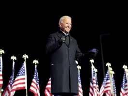 Joe Biden in front of American flags, black background | Licas News