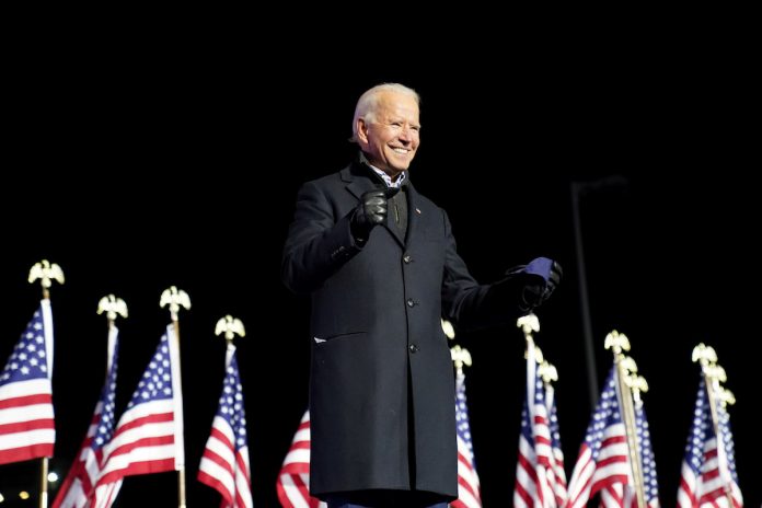 Joe Biden in front of American flags, black background | Licas News