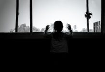 Black and white photo of back of child looking out of a large window