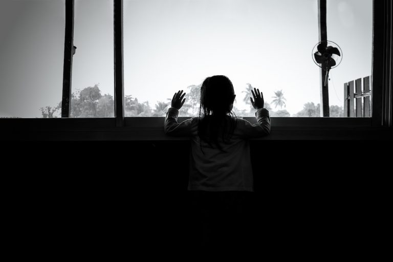 Black and white photo of back of child looking out of a large window