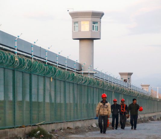Workers walk by the perimeter fence in Xinjiang