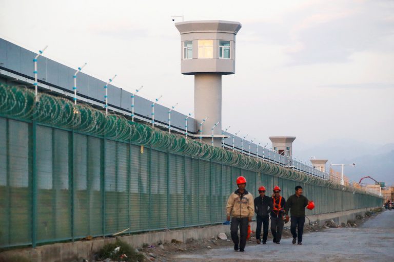 Workers walk by the perimeter fence in Xinjiang