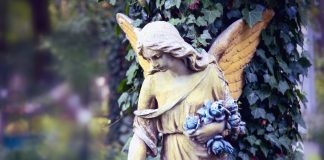 Vintage image of a sad angel against the background of leaves (fragment)