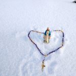 Statue of Virgin Mary and Rosary with snow in the background at the top of Mount Everest