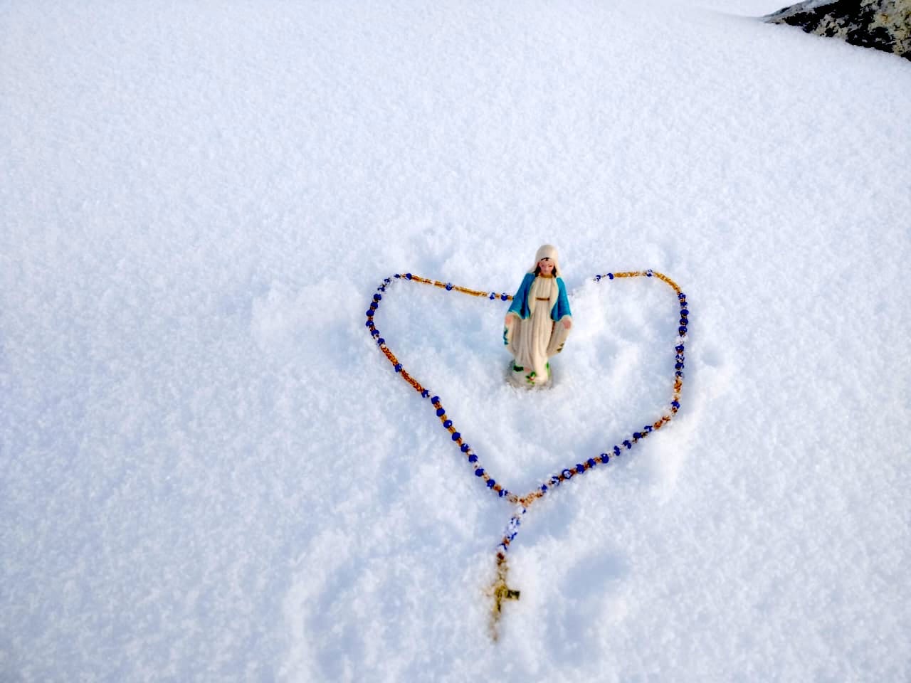 Statue of Virgin Mary and Rosary with snow in the background at the top of Mount Everest