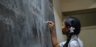 Indian girl writing on blackboard with chalk