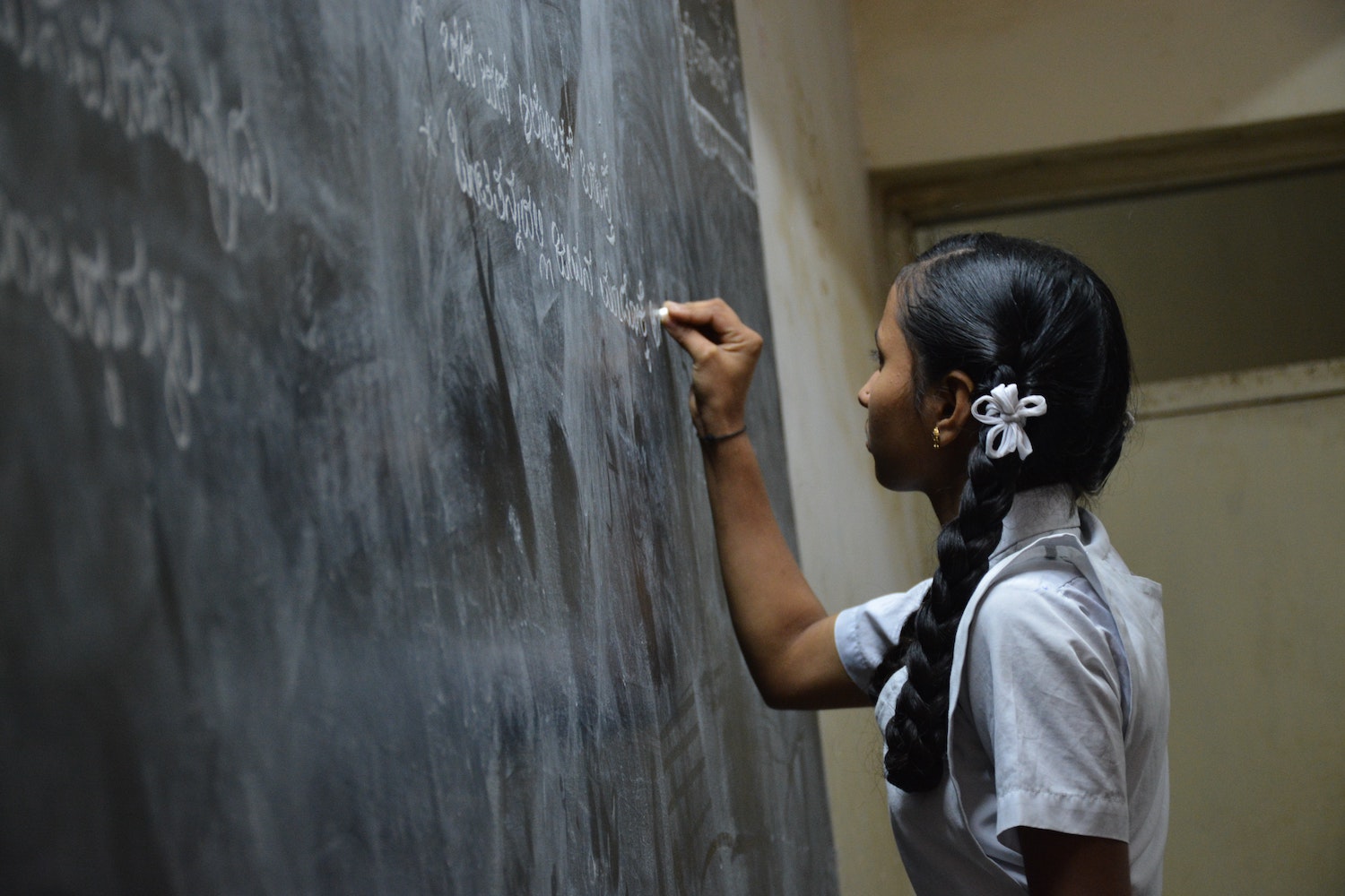 Indian girl writing on blackboard with chalk