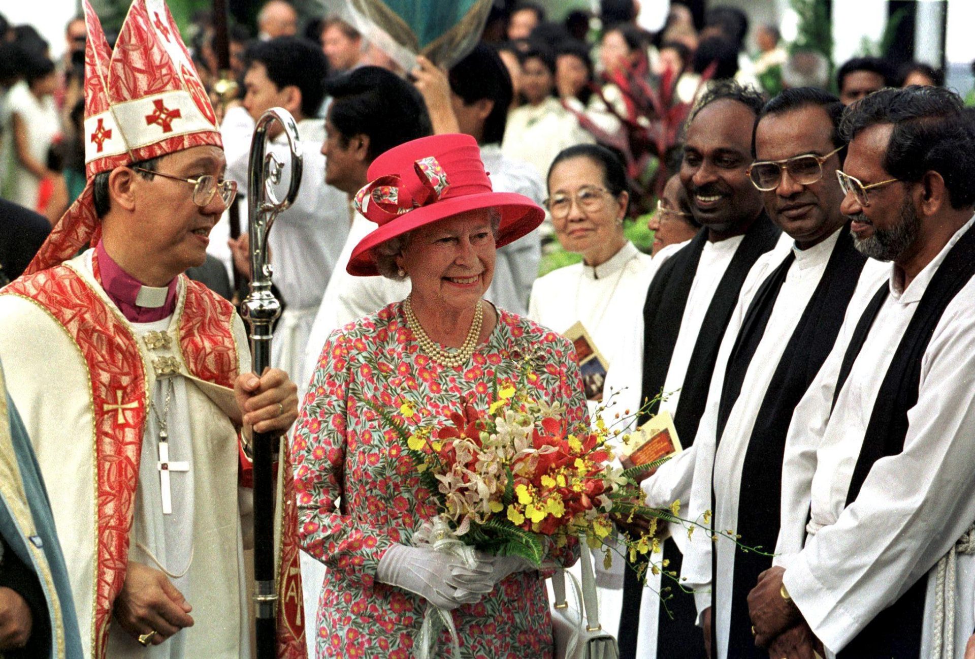 Queen Elizabeth II​ holding a bouquet of flowers while meeting priests in Malaysia