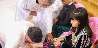 Cardinal Charles Maung Bo washing the feet of a young girl wearing indigenous clothing