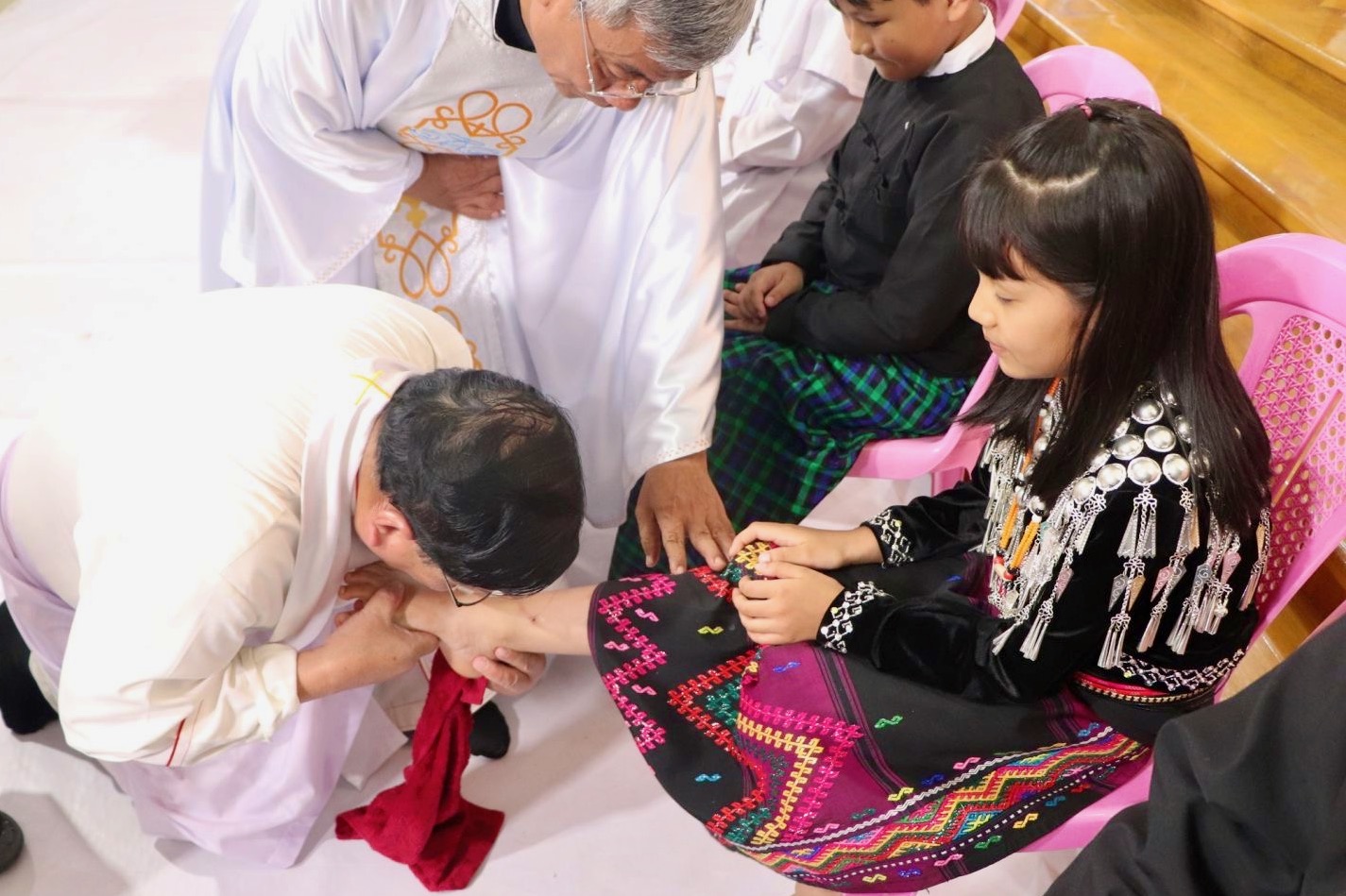 Cardinal Charles Maung Bo washing the feet of a young girl wearing indigenous clothing