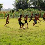 Children playing football in a grass field in Bangladesh