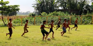 Children playing football in a grass field in Bangladesh