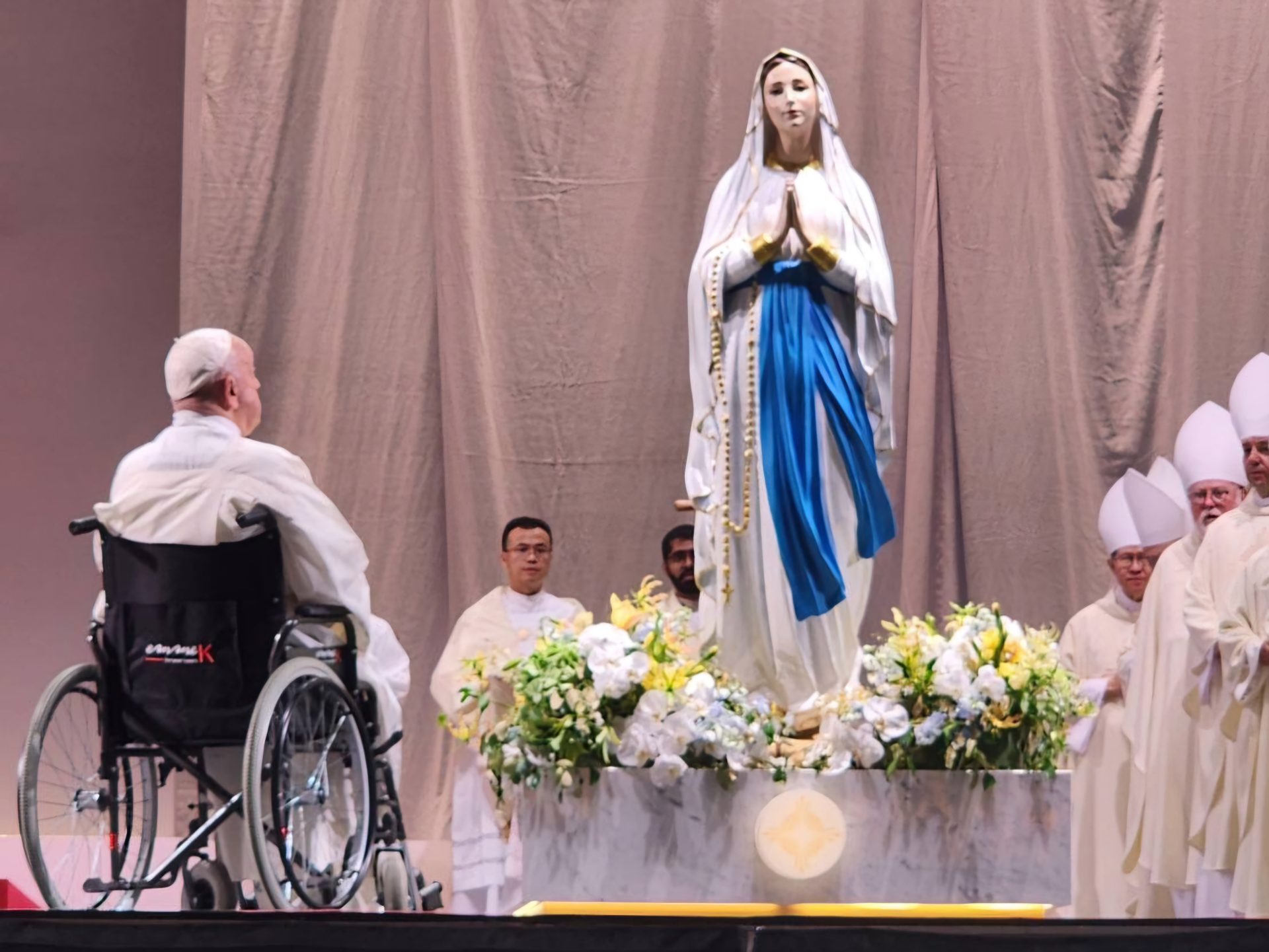 Pope Francis sitting in a wheelchair in front of the statue of the Virgin Mary in Singapore