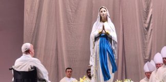 Pope Francis sitting in a wheelchair in front of the statue of the Virgin Mary in Singapore