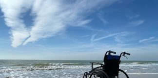 An empty wheelchair on a sandy beach on a sunny day