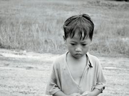 Black and white photo of a poor boy in rural setting in Asia