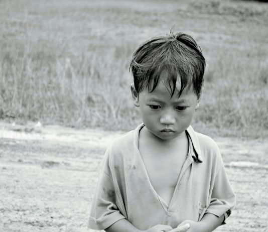 Black and white photo of a poor boy in rural setting in Asia