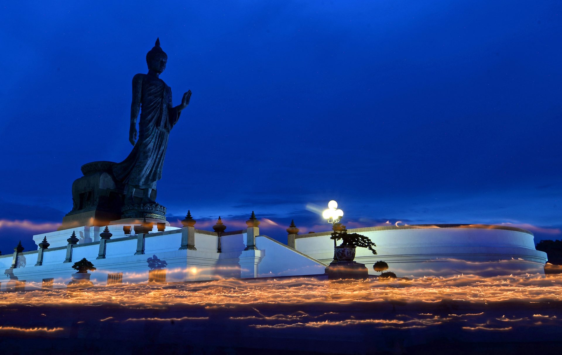 Visakha Bucha Day procession at Buddha Monthon in Nakhon Pathom, Thailand, with candle streaks against the dark blue evening sky