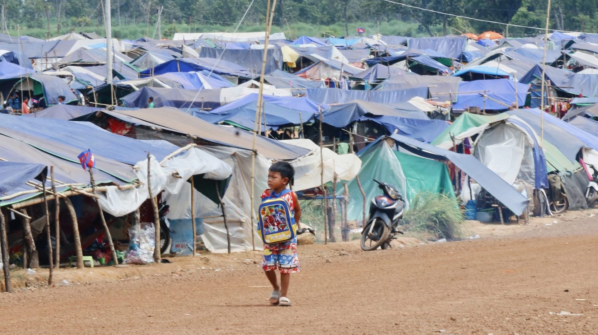 A young boy walks past rows of makeshift tents at a refugee camp near the Cambodia–Thailand border.