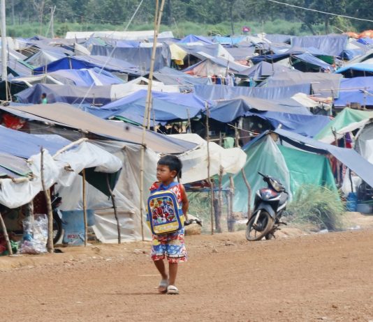 A young boy walks past rows of makeshift tents at a refugee camp near the Cambodia–Thailand border.